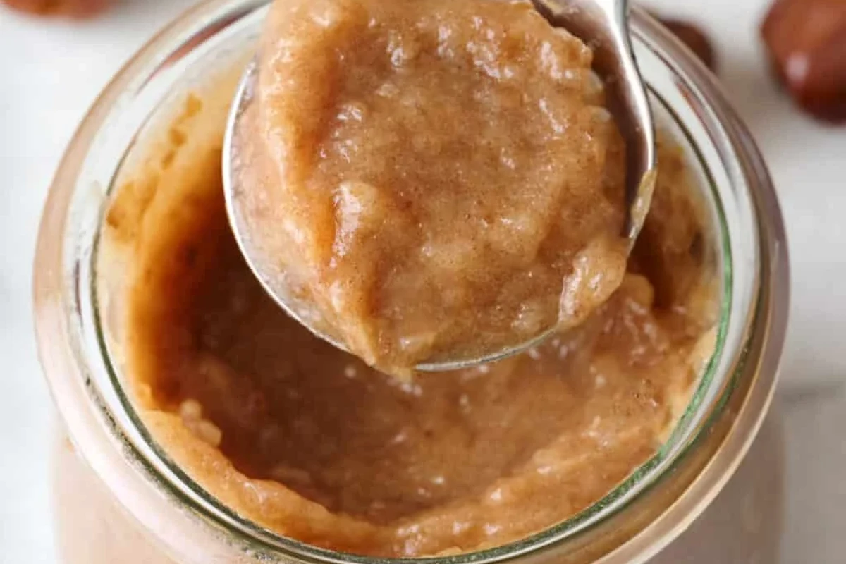Homemade date paste in a bowl with dates, a blender, and a spoon on a kitchen counter