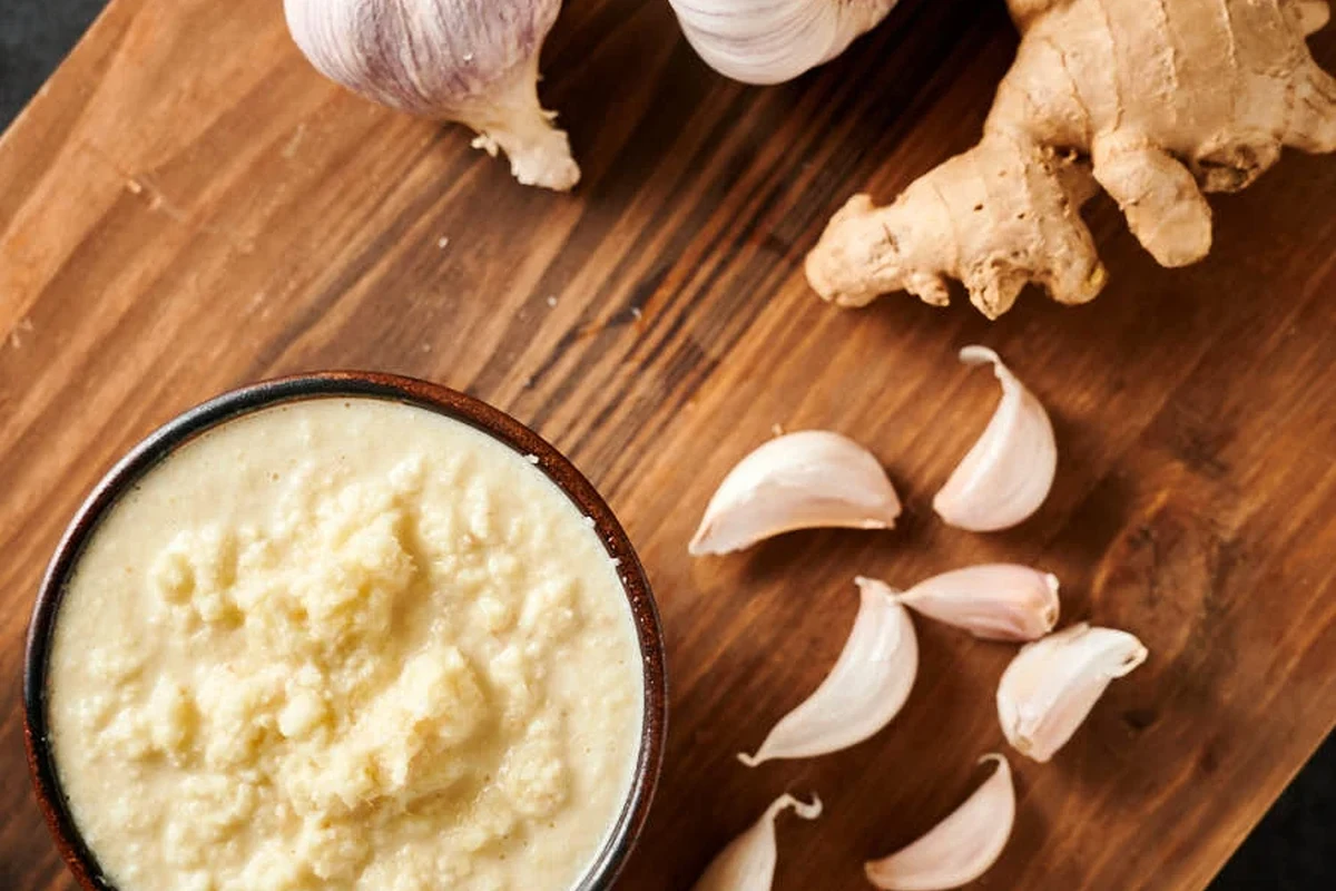 Fresh ginger and garlic paste in a small glass jar beside peeled ginger and garlic cloves