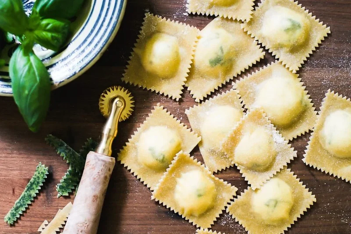Fresh homemade ravioli dough rolled thin with flour, eggs, and pasta tools on a kitchen counter