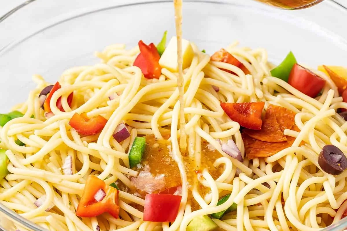 Bowl of spaghetti pasta salad with vegetables, herbs, and dressing on a kitchen counter