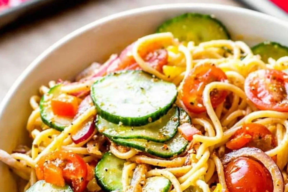 Bowl of spaghetti pasta salad with vegetables, herbs, and dressing on a kitchen counter