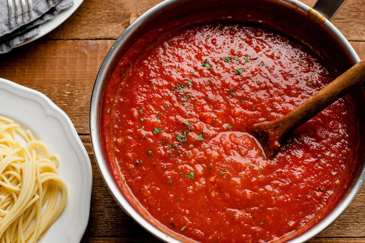 Tomato sauce made from tomato paste in a saucepan with herbs and a wooden spoon