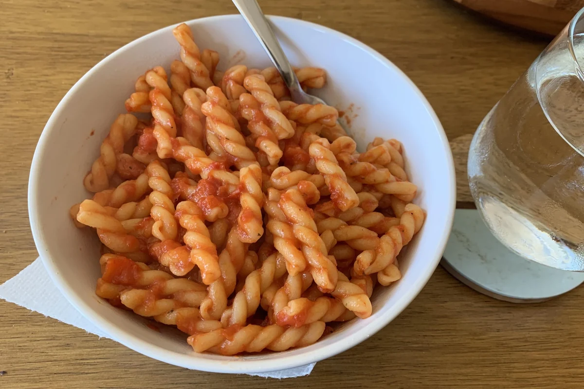 Bowl of pasta with tomato sauce, cream sauce, and measuring cup on a kitchen counter