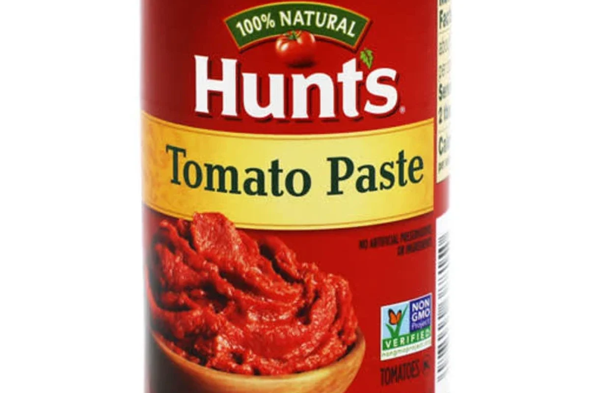 Measuring 6 ounces of tomato paste in a cup beside pasta sauce ingredients
