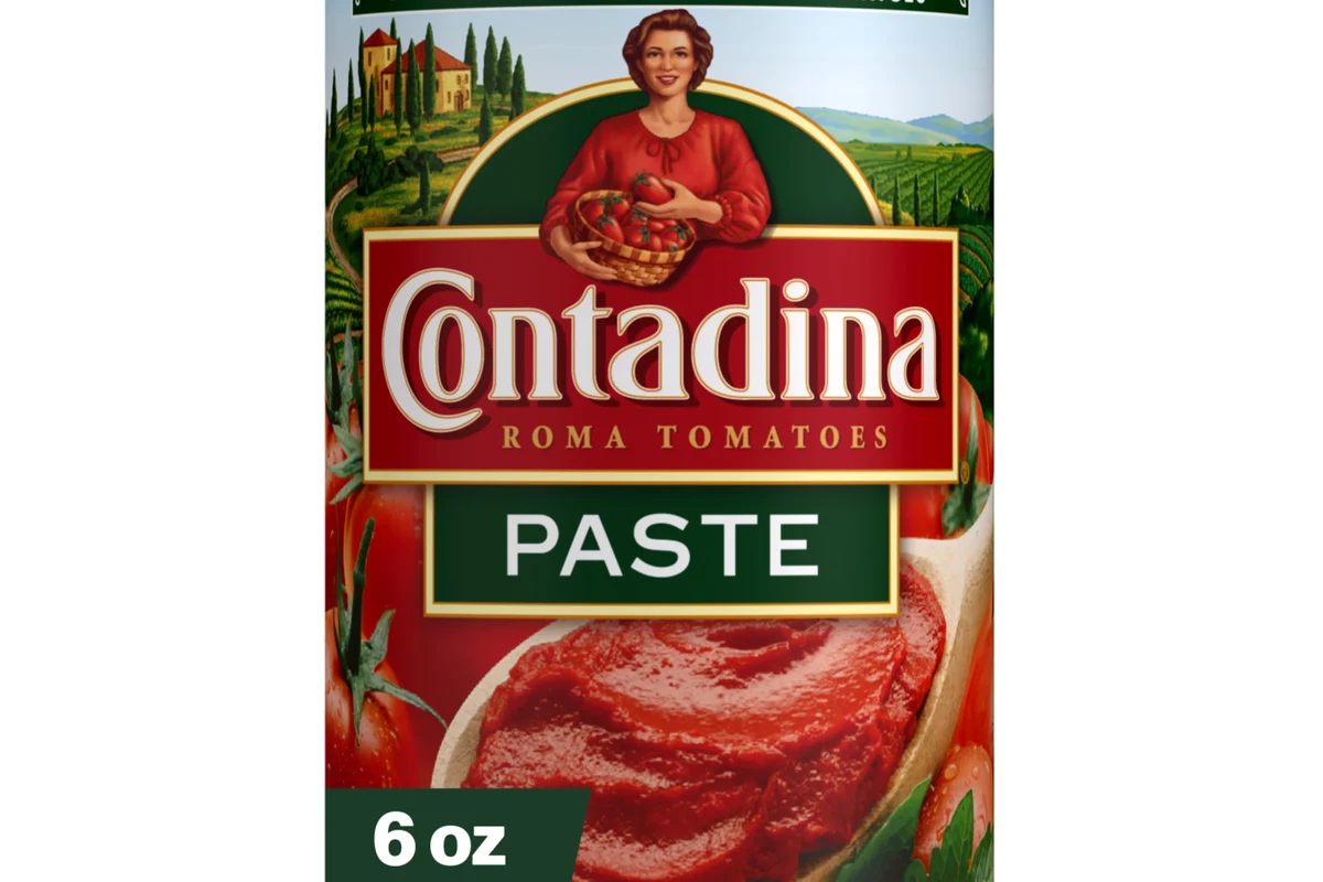 Measuring 6 ounces of tomato paste in a cup beside pasta sauce ingredients