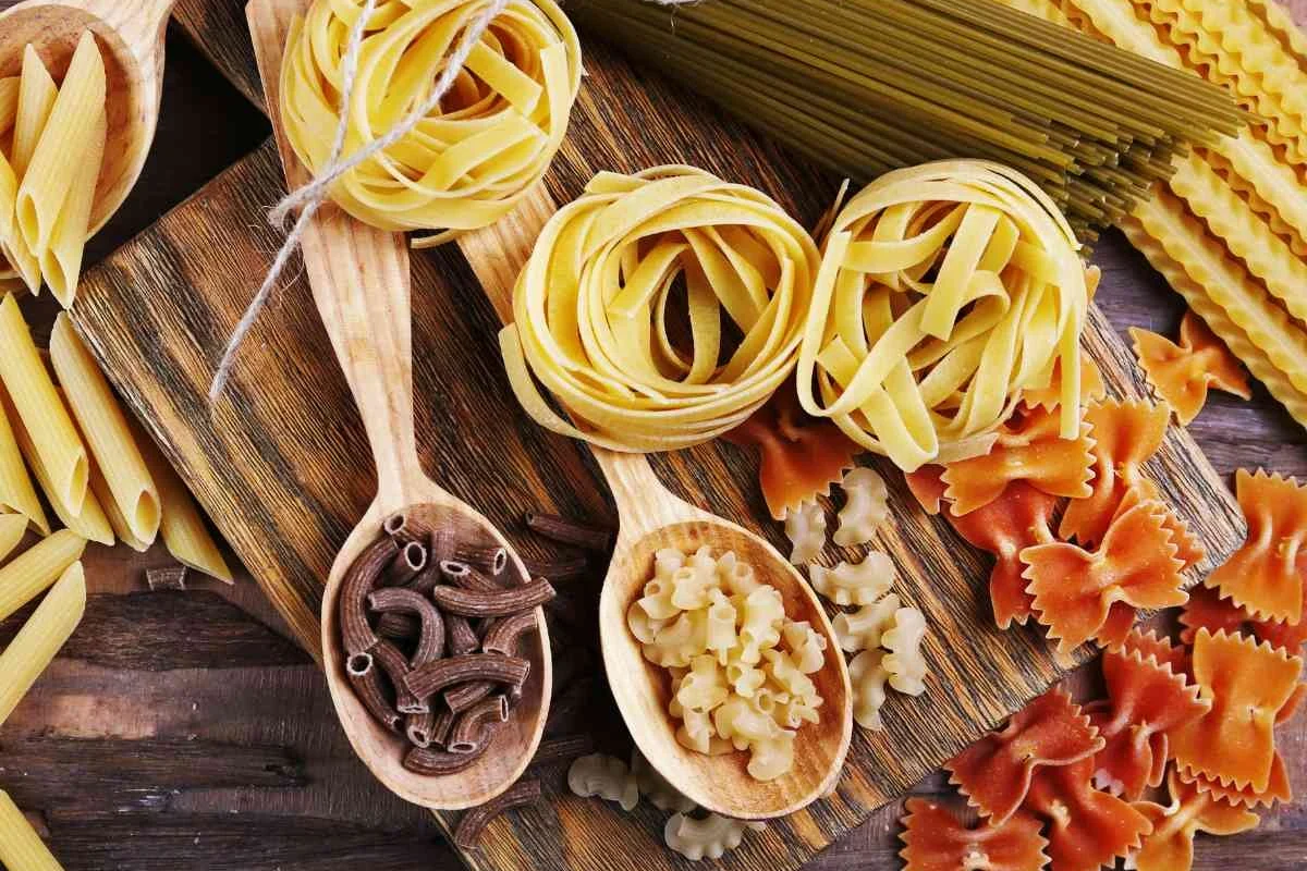 Dry pasta cups and a kitchen scale beside a bowl of uncooked spaghetti on a kitchen counter
