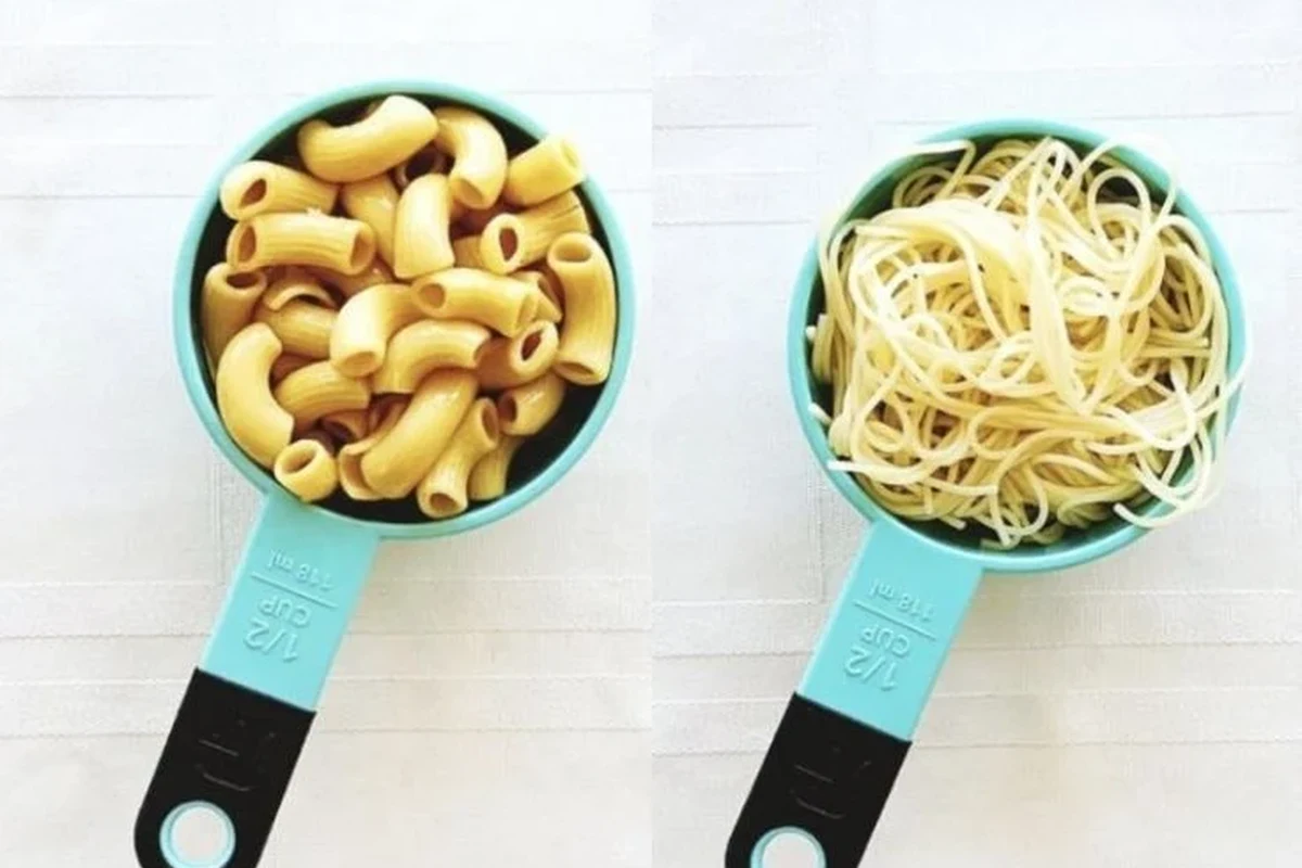 Measuring dry pasta in a cup beside a pot of cooked pasta in a home kitchen