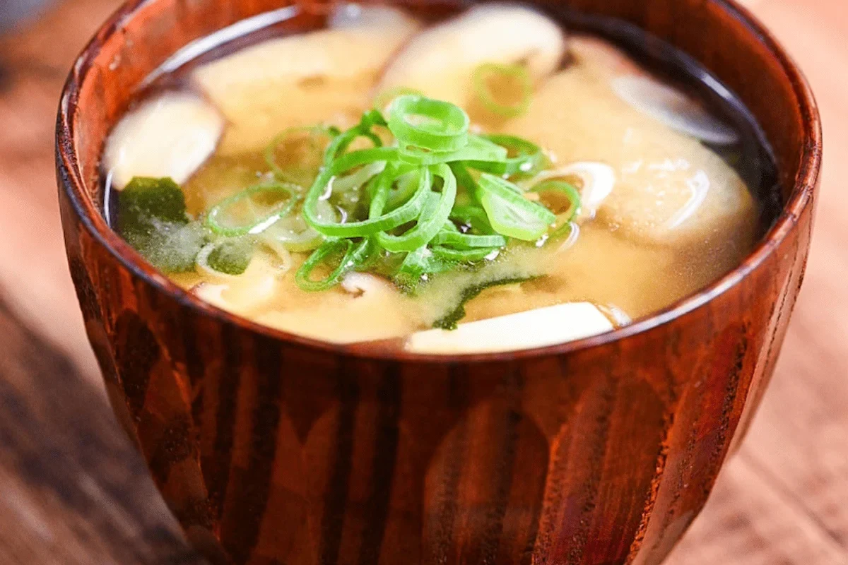 Bowl of miso paste with soybeans, rice, salt, and wooden spoon on a kitchen counter