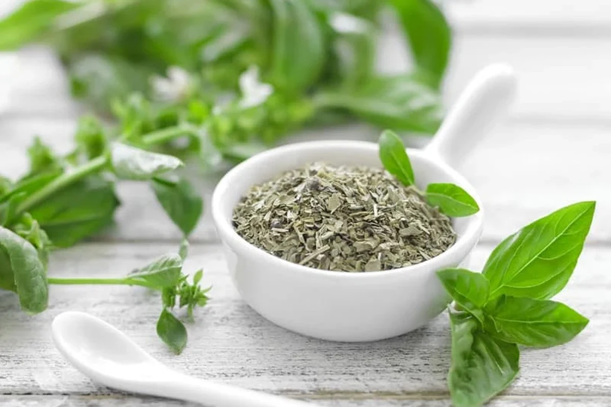 Basil paste beside fresh basil leaves and measuring spoons on a kitchen counter