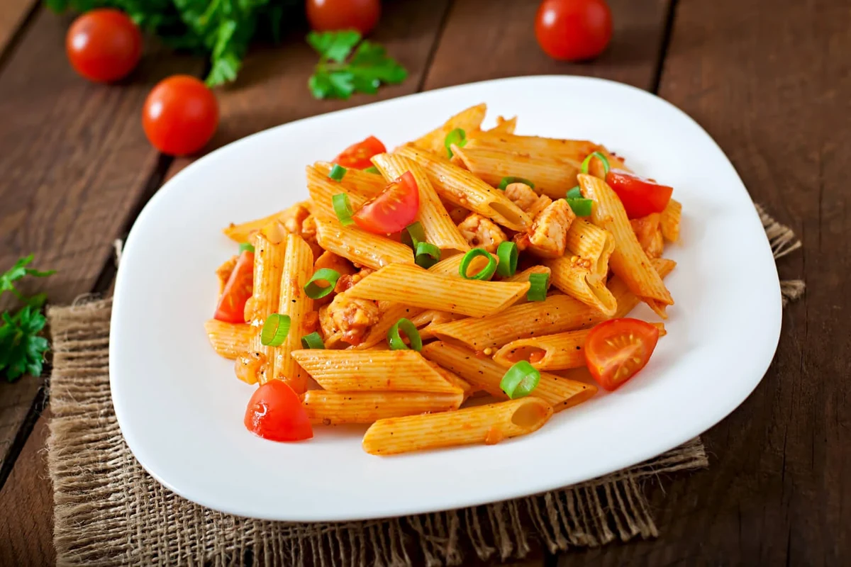 Dry penne pasta portioned in a bowl beside measuring cups in a bright home kitchen