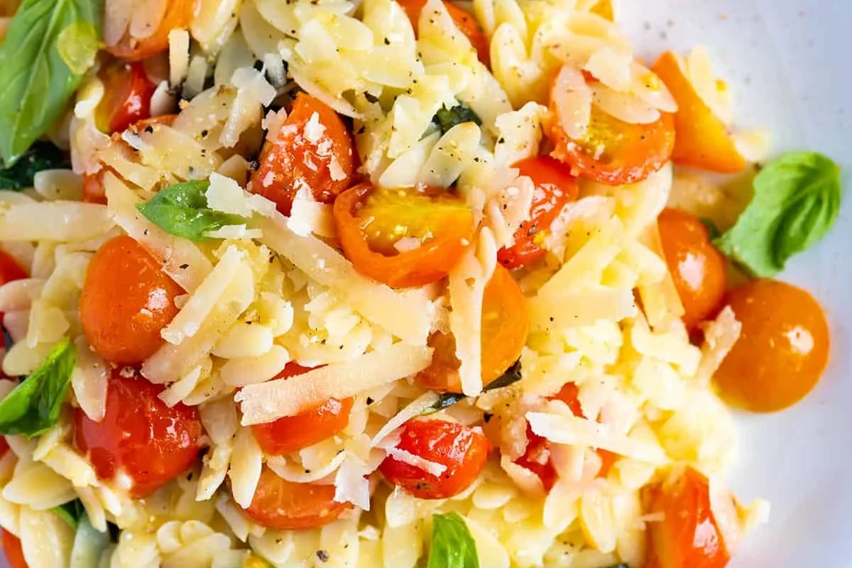 Bowl of orzo pasta with vegetables and herbs on a kitchen table
