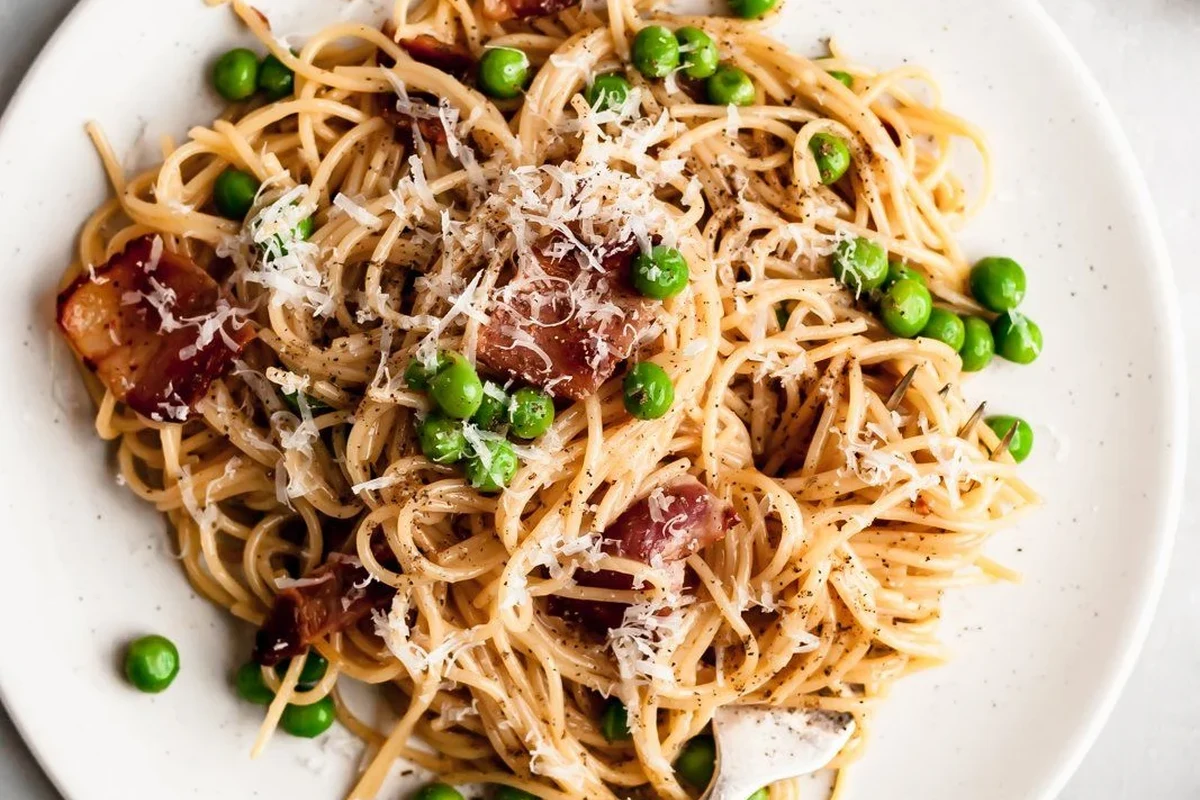 A bowl of pasta carbonara with eggs, cheese, and pancetta on a kitchen table