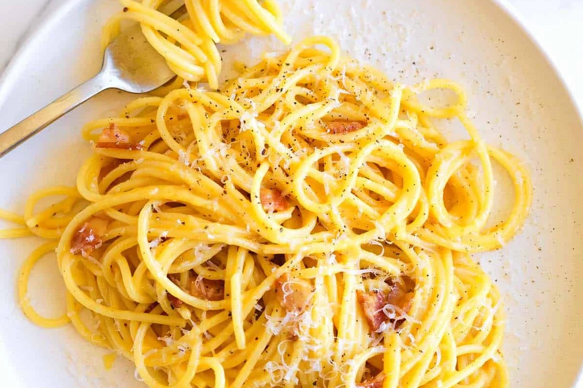 A bowl of pasta carbonara with eggs, cheese, and pancetta on a kitchen table