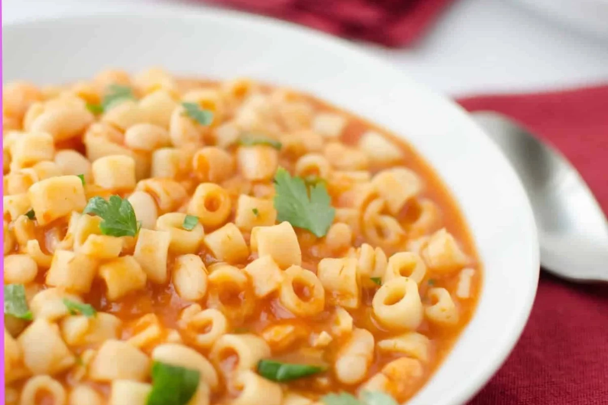 A bowl of pasta fagioli soup with beans, pasta, and vegetables on a kitchen table