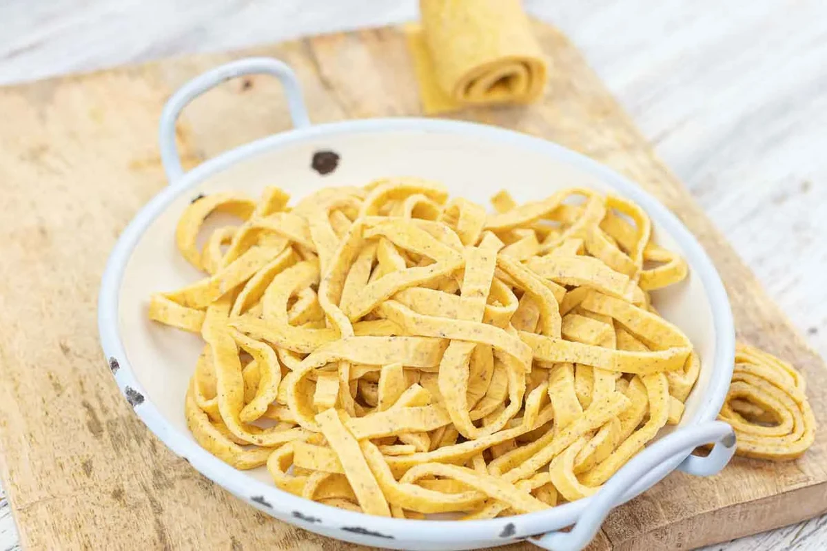 Bowl of pasta with vegetables, olive oil, and lean protein on a kitchen table
