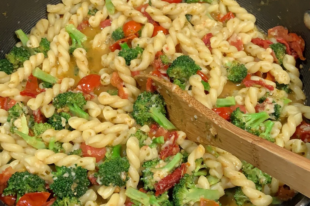 Pregnant person eating a balanced bowl of pasta with vegetables and protein in a home kitchen