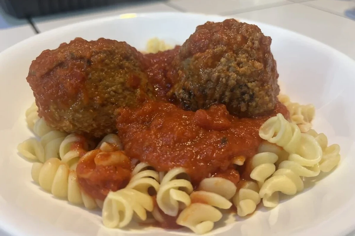 Bowl of pasta and meatballs with tomato sauce and a side of vegetables in a home kitchen