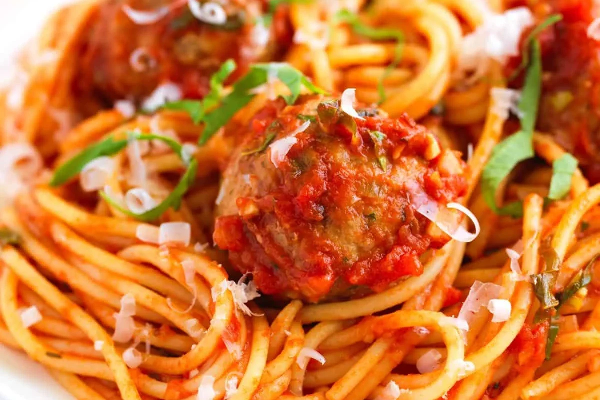 Bowl of pasta and meatballs with tomato sauce and a side of vegetables in a home kitchen