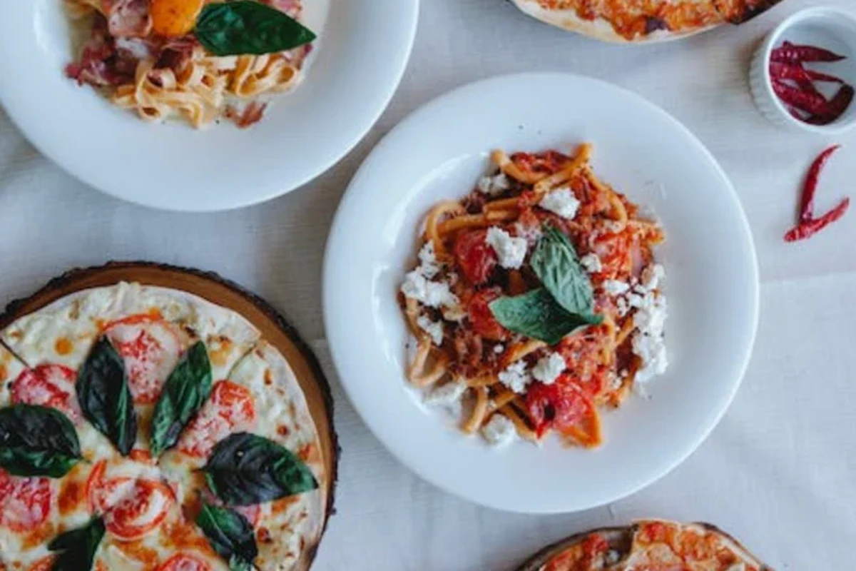 A bowl of whole grain pasta and a thin-crust vegetable pizza on a kitchen table