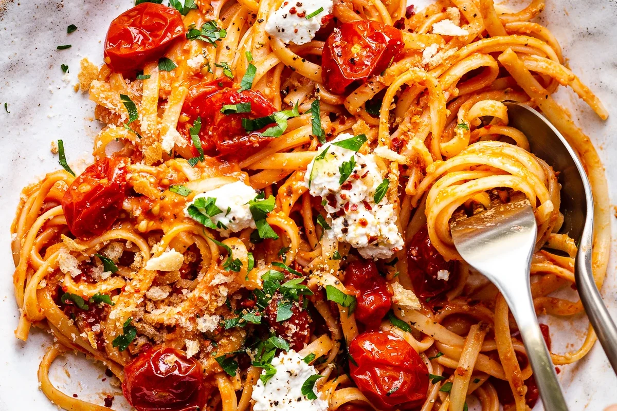 Bowl of pasta with tomato sauce, basil, and vegetables on a kitchen table