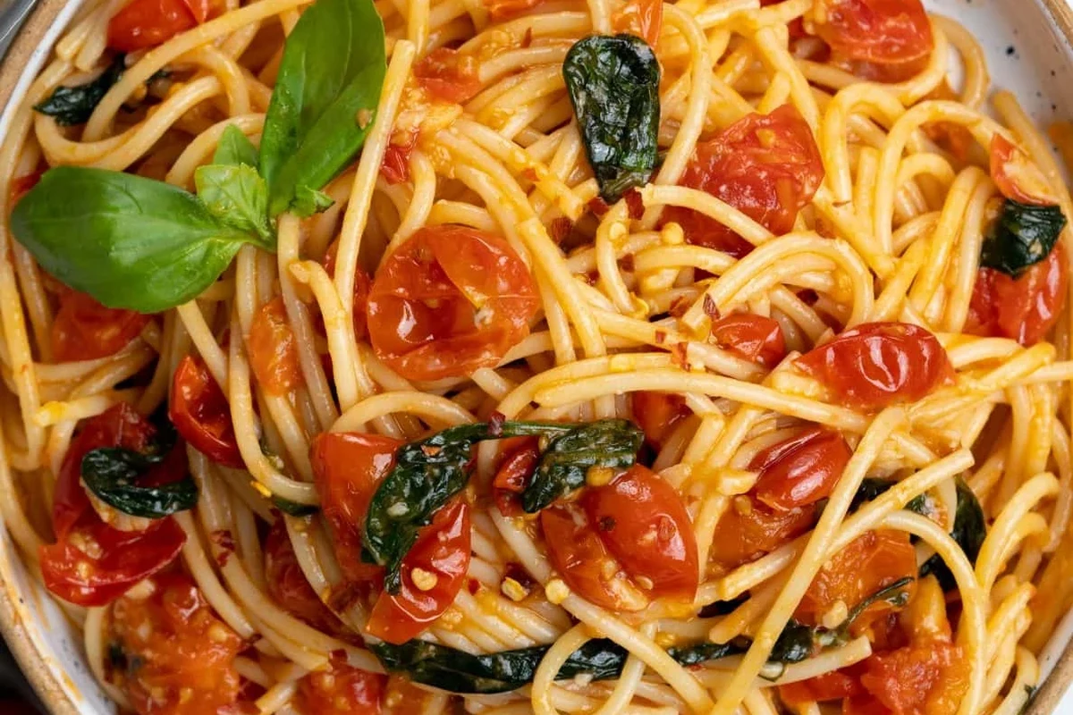 Bowl of pasta with tomato sauce, basil, and vegetables on a kitchen table