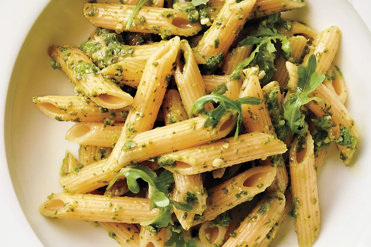 Bowl of penne pasta with vegetables and tomato sauce on a kitchen table