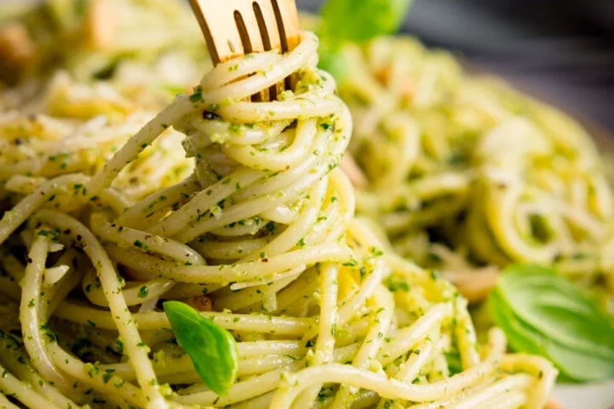 Bowl of pesto pasta with vegetables and herbs on a kitchen table