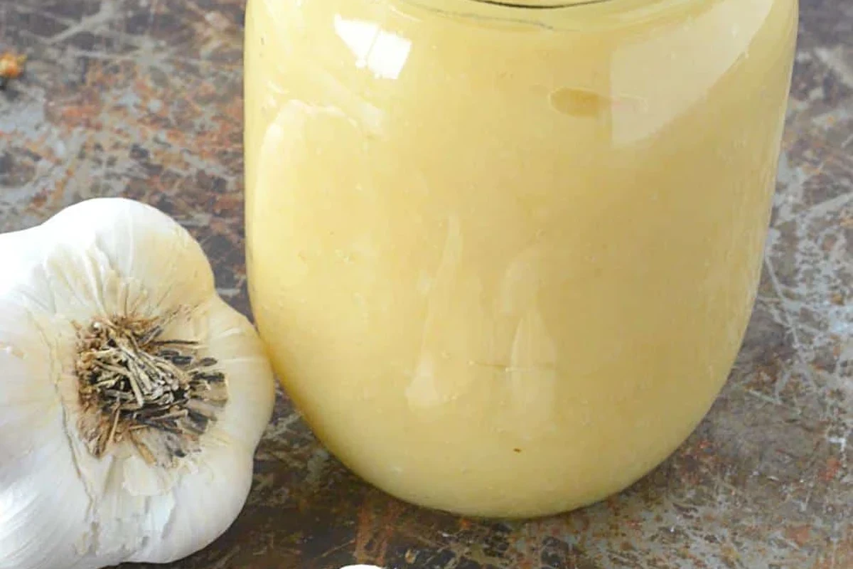 Fresh garlic cloves, knife, and smooth garlic paste in a small bowl on a kitchen counter