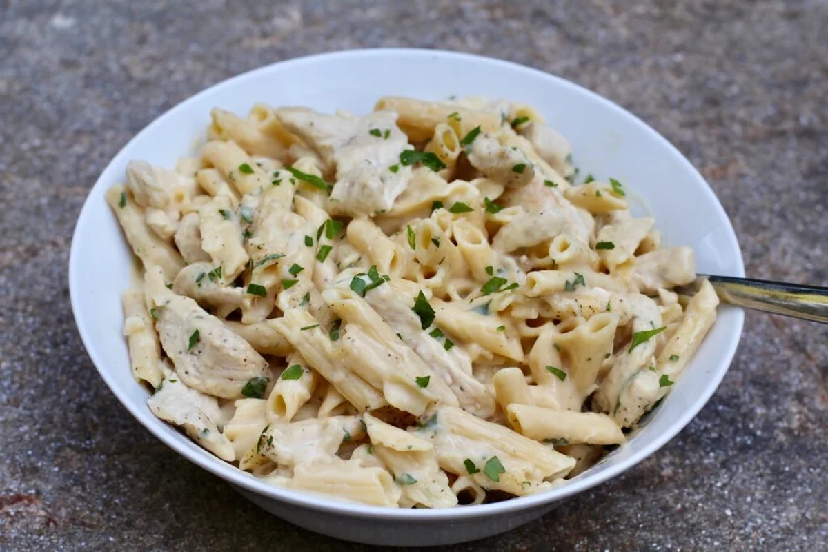Creamy white sauce pasta in a bowl with fork, herbs, and a kitchen counter background