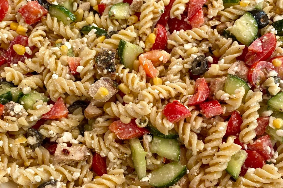 Bowl of protein pasta with tomato sauce, vegetables, and herbs on a kitchen table