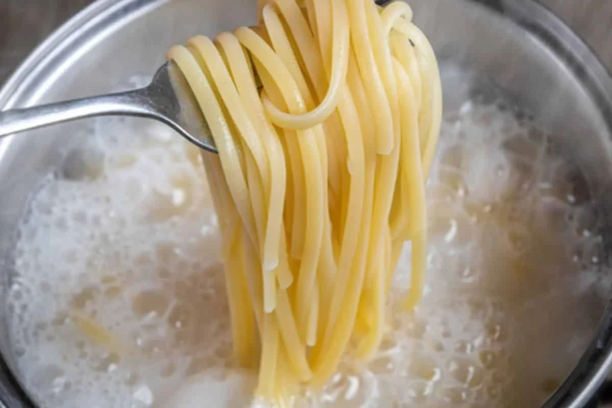 Leftover pasta being reheated gently in a skillet with sauce and steam