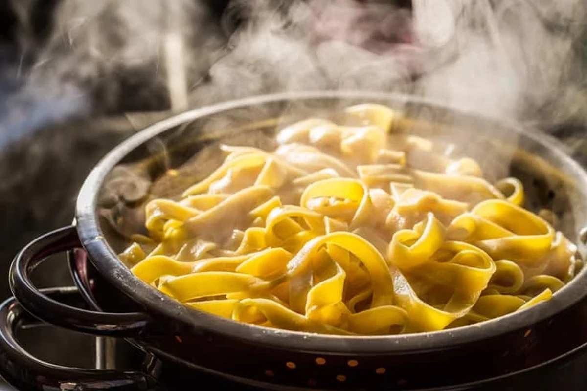 Leftover pasta being reheated gently in a skillet with sauce and steam