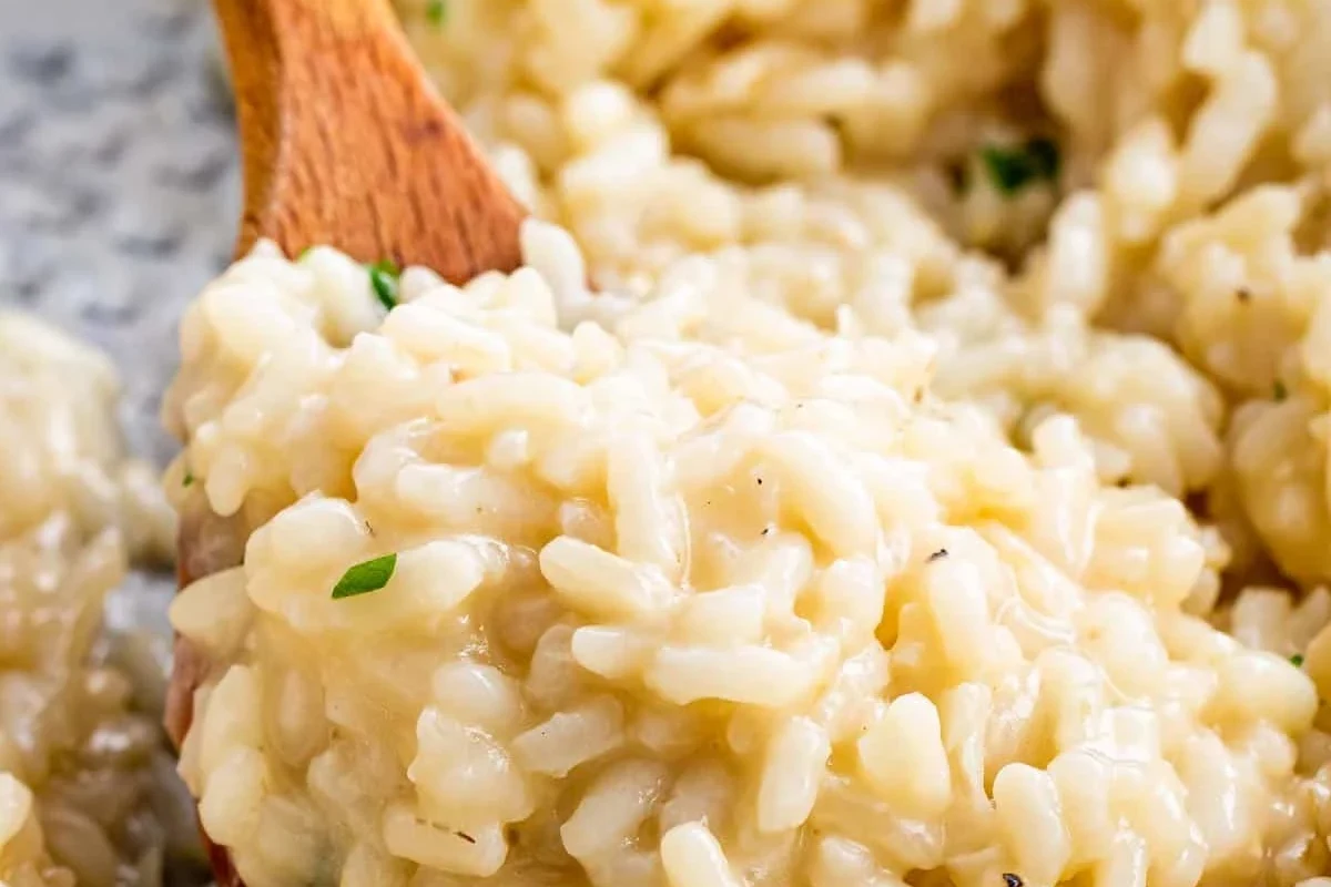 Creamy risotto in a bowl beside uncooked short-grain rice on a kitchen counter
