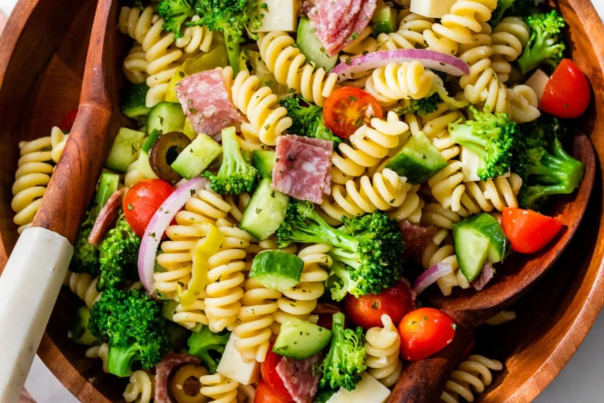 Pasta salad served with grilled chicken, green salad, bread, and fruit on a bright table