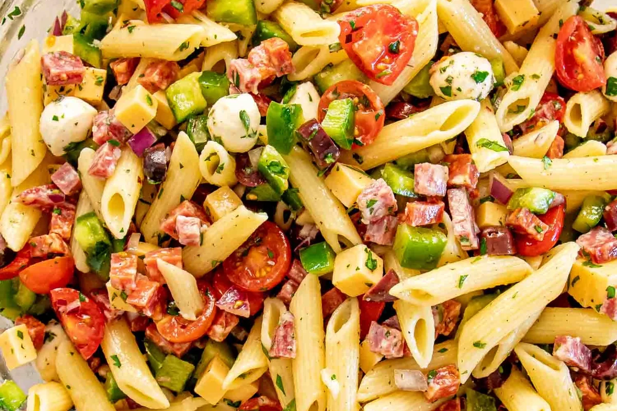 Pasta salad served with grilled chicken, green salad, bread, and fruit on a bright table