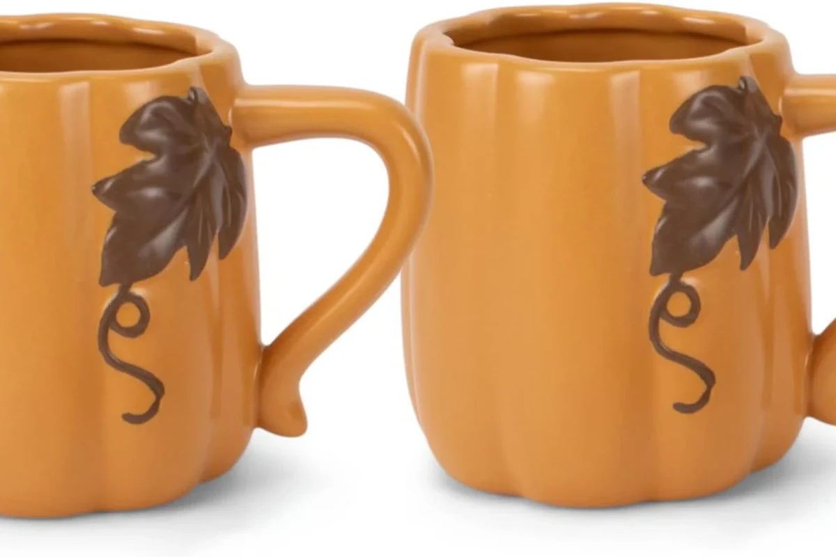 Ceramic coffee mugs with printed designs and one hand washing in a kitchen sink