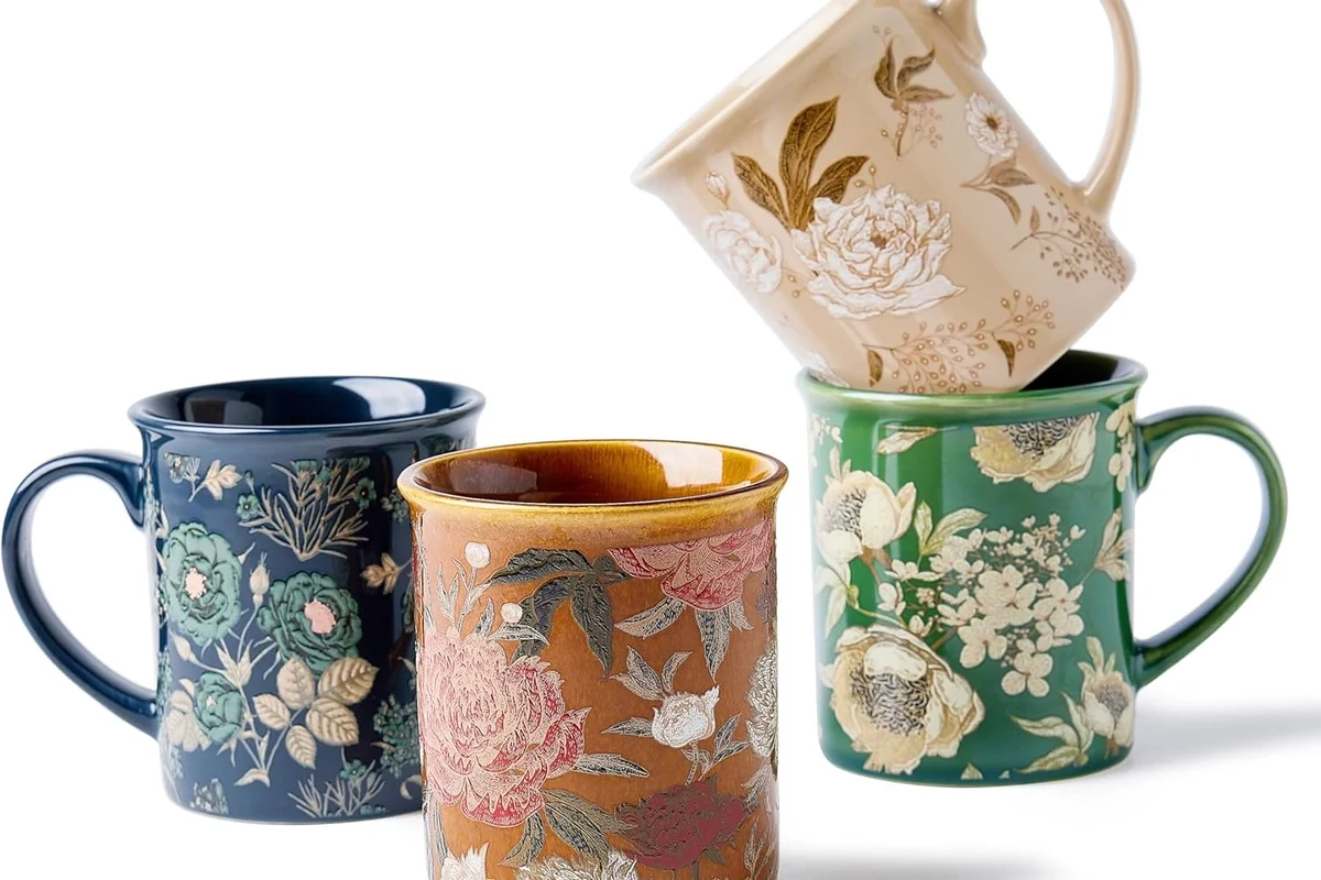 Ceramic coffee mugs with printed designs and one hand washing in a kitchen sink