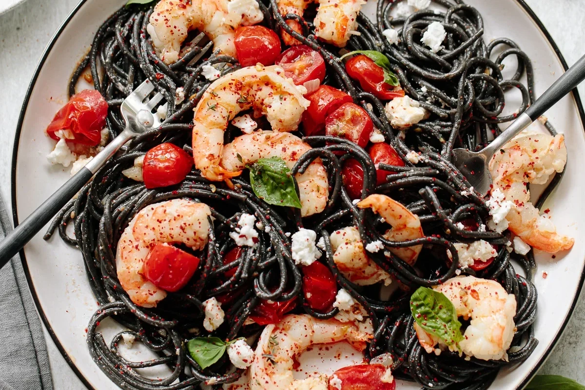 Black squid ink pasta served with seafood and herbs in a bright home kitchen