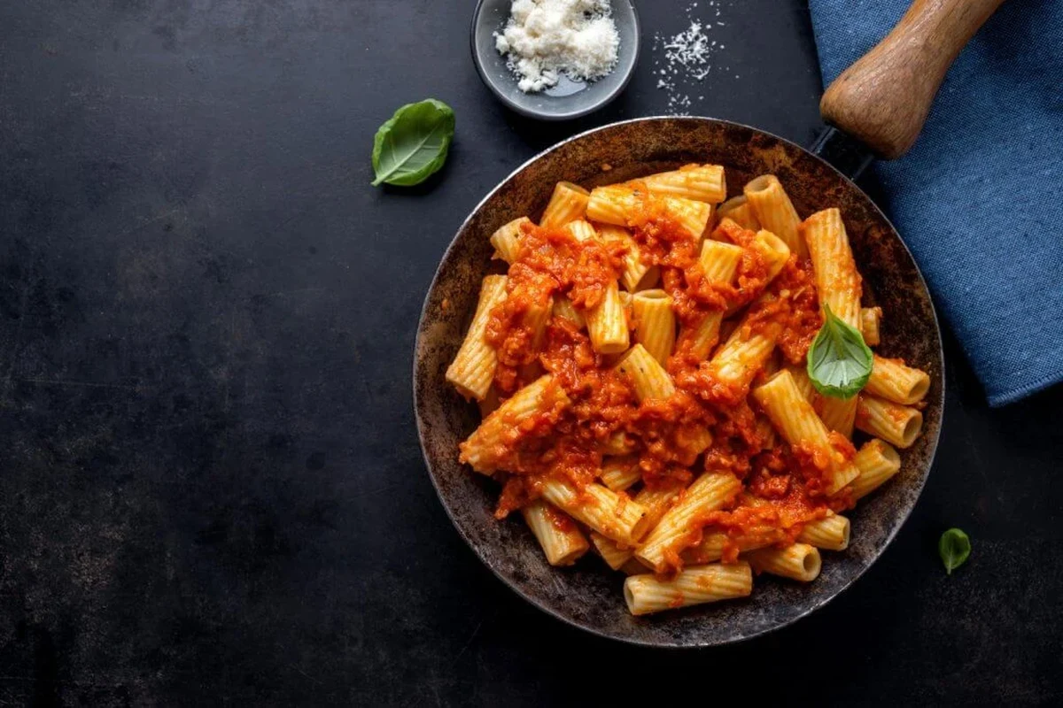 A pot of pasta sauce simmering on a stove with a spoon and ingredients nearby