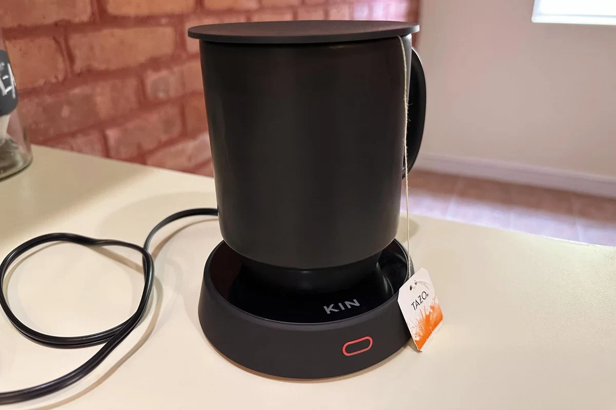 Coffee mug warmer on a kitchen counter beside a ceramic mug of hot coffee
