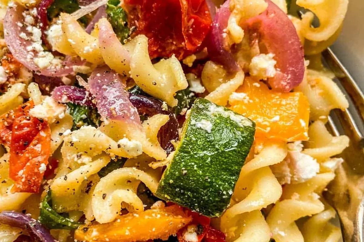 Bowl of veggie pasta with tomato sauce, fresh vegetables, and herbs in a bright home kitchen