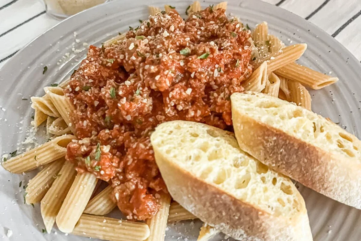 Bowl of whole wheat pasta with vegetables and tomato sauce on a kitchen table
