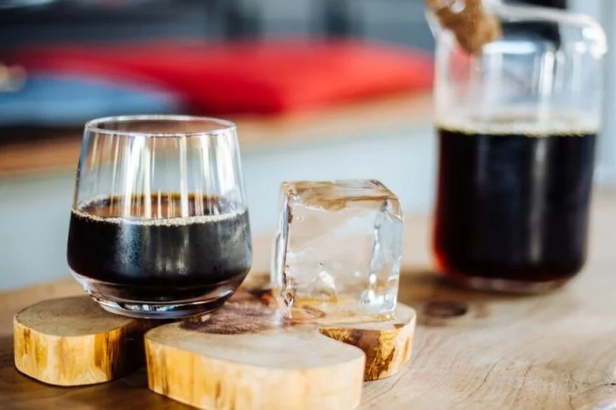 Glass of black cold brew coffee beside a kitchen counter and brewing jar