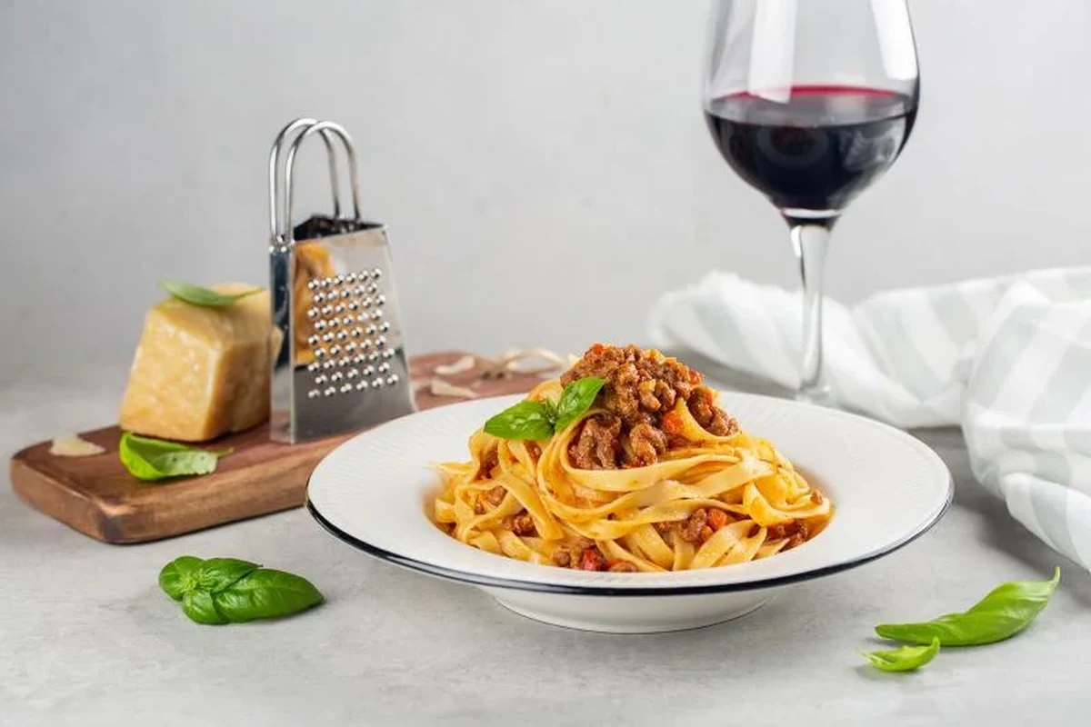 Wine glasses beside pasta dishes with marinara, Alfredo, pesto, and lasagna on a dinner table