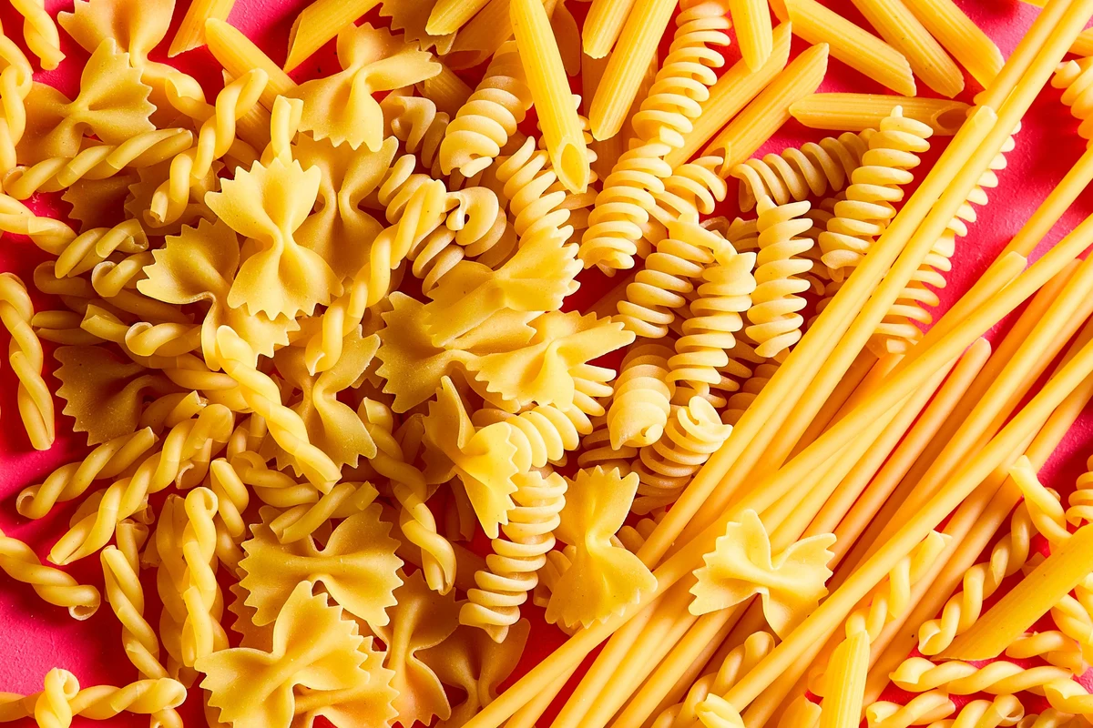 Bowl of dry and cooked pasta on a kitchen counter with a wooden spoon
