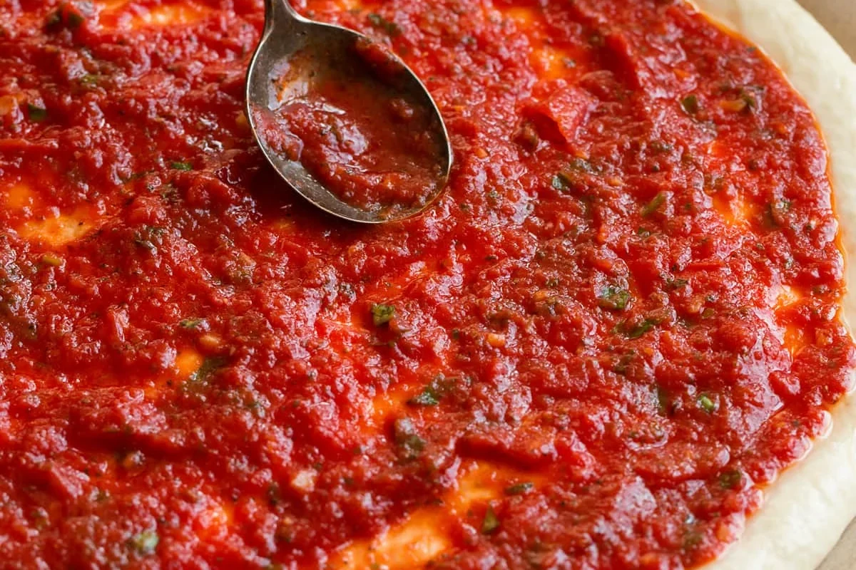 Jar of pasta sauce beside a homemade pizza with cheese and toppings